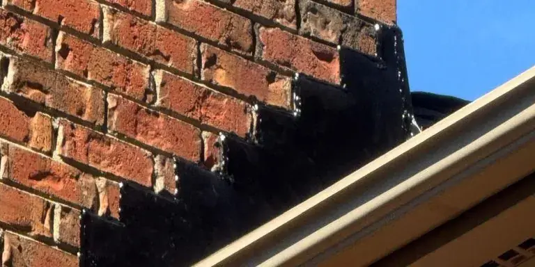 Step flashing along a brick chimney that has been coated over with black roofing cement instead of being properly replaced